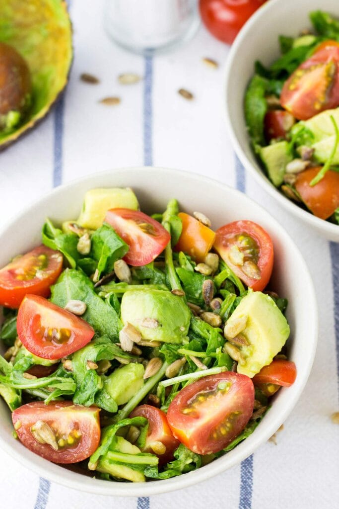 The bowl of salad is on a blue and white striped table cloth with salt and tomato | Hurry The Food Up