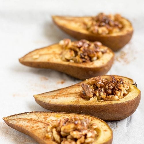 Four pear halves stuffed with walnuts and cinnamon are laid on a white surface | Hurry The Food Up