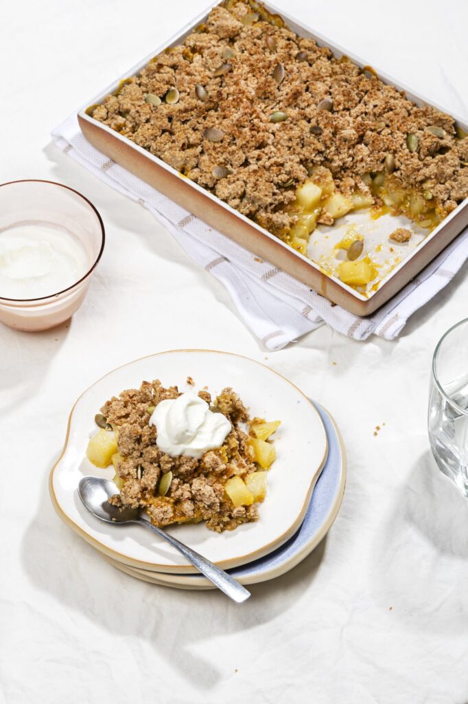 A serving of healthy breakfast crisp alongside a tray of the bake and a bowl of yoghurt. | Hurry The Food Up