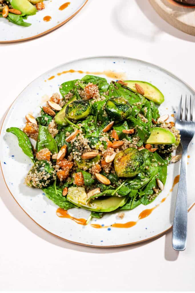 A plate of smashed brussel sprouts and quinoa salad, drizzled with dressing. A jug of dressing is nearby. | Hurry The food Up