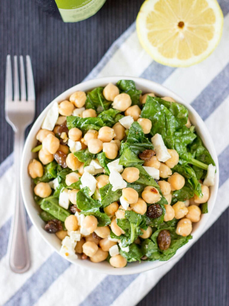 Chickpea Spinach Salad from a bird's eye view, with a blue and white striped placemat underneath it and a wedge of lemon in background | Hurry The Food Up