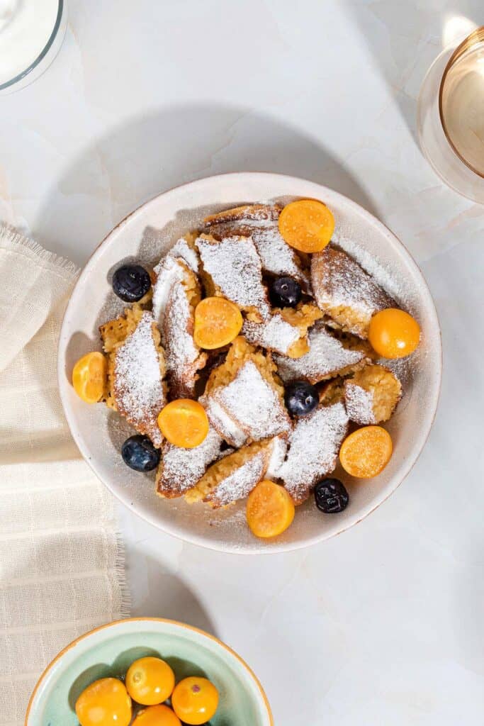 A birds eye view of a bowl of schmarrn breakfast, with fruit and yogurt, on a white marble surface | Hurry The Food Up