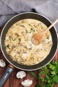 Cooked mushrooms in a big pan. Next to it, there are grey tablecloth, a bunch of parsley, and two pieces of mushrooms | Hurry The Food Up