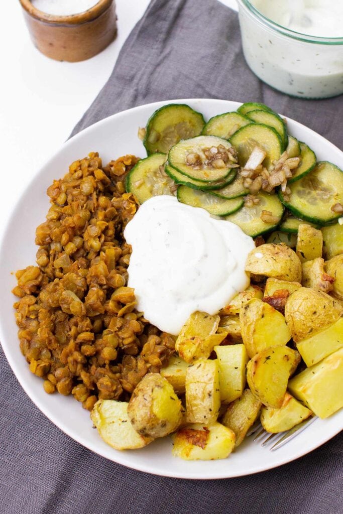 The Buddha bowl is served with cucumber salad on the table on a plate with tea towel, salt and sauce #vegetable broth #brown lentils | hurrythefoodup.com