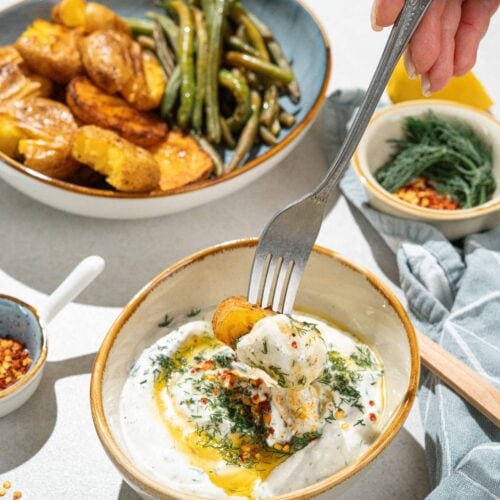 The bowl with smashed potatoes and green beans is on the grey surface. Near it, there are smaller bowls with feta dipping sauce, sweet paprika flakes, dill etc | Hurry The Food Up