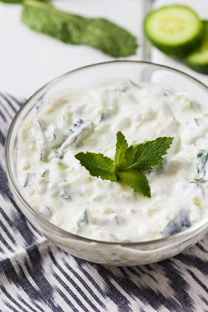 Cucumber Raita is served in the bowl with mint leaves and cucumber slices | Hurry The Food Up