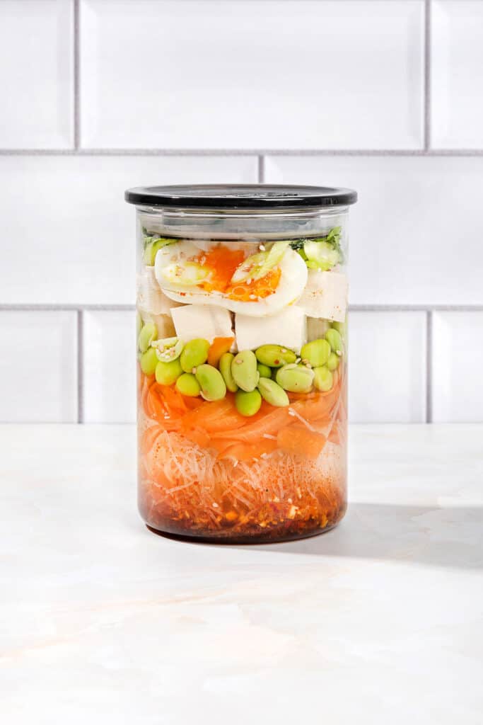 A sealed jar of all the constituent ingredients of an easy homemade ramen noodle soup, on a white surface | Hurry The Food Up