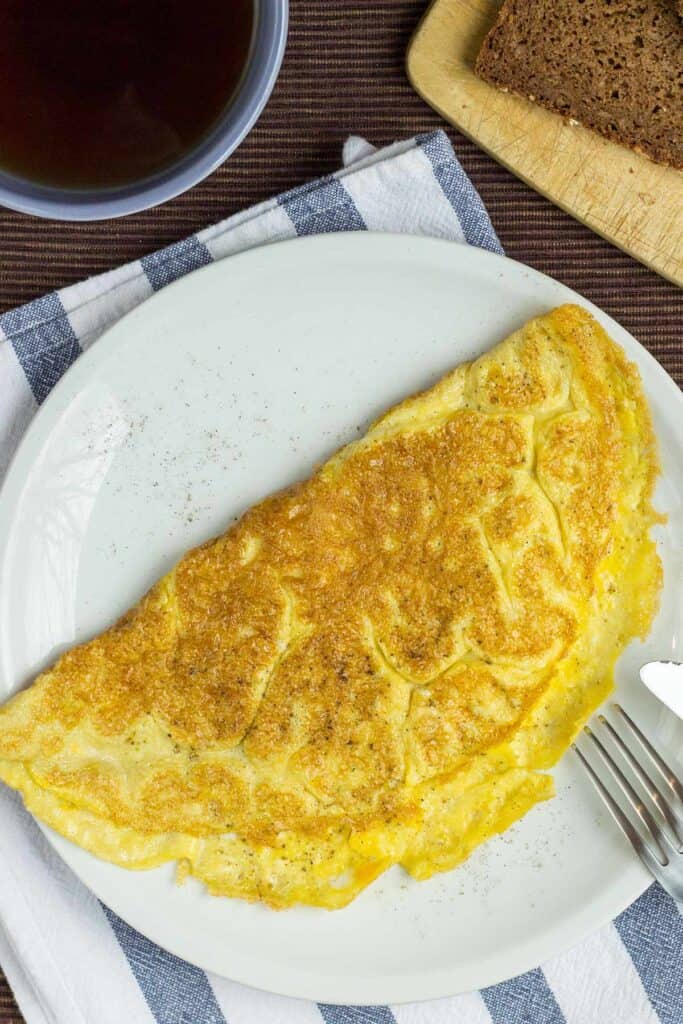 An omelette is seen from a bird's eye view, resting on a white plate, with a mug of coffee in the upper left hand corner. | Hurry The Food Up