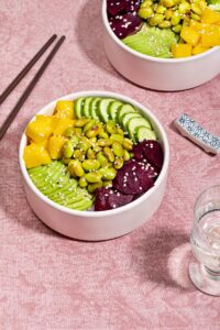 A vegetarian poke bowl is in the centre of the image, alongside a pair of chopsticks, another bowl visible in the top corner.