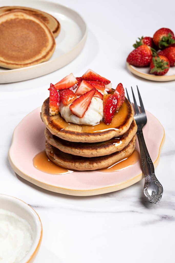 The lentil pancakes are served on the plate with fork and topped with strawberries, maple syrup and low fat greek yogurt | Hurry The Food Up