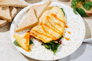 High Protein Omelette, topped with sriracha, salt and black pepper which is on the light plate. Two pieces of bread are on it as well | Hurry The Food Up