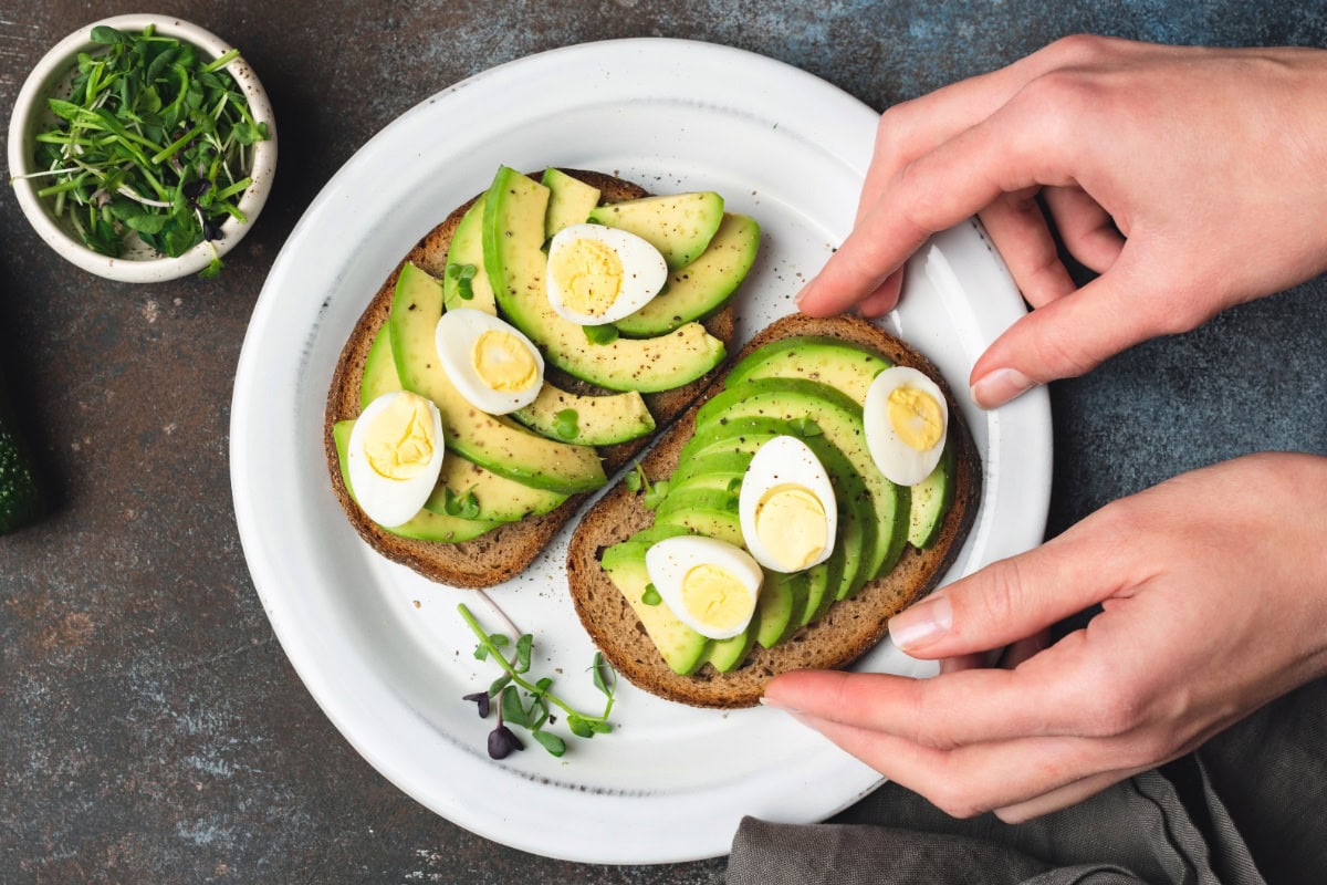 The toasts with avocado and quail eggs are on the white plate | Hurry The Food Up