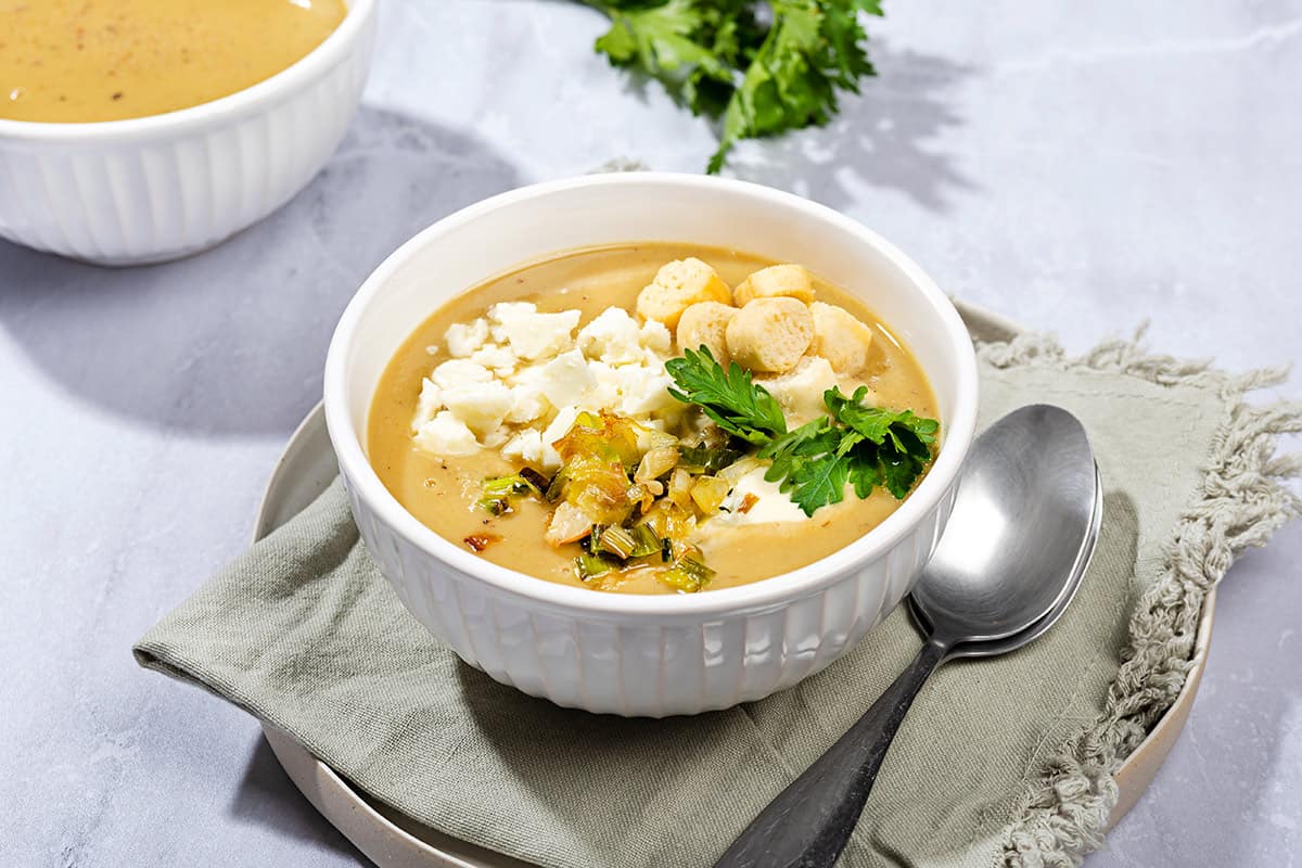 A close up shot of leek and potato soup served in a bowl, placed on a grey napkin with a spoon beside it. | Hurry The Food Up