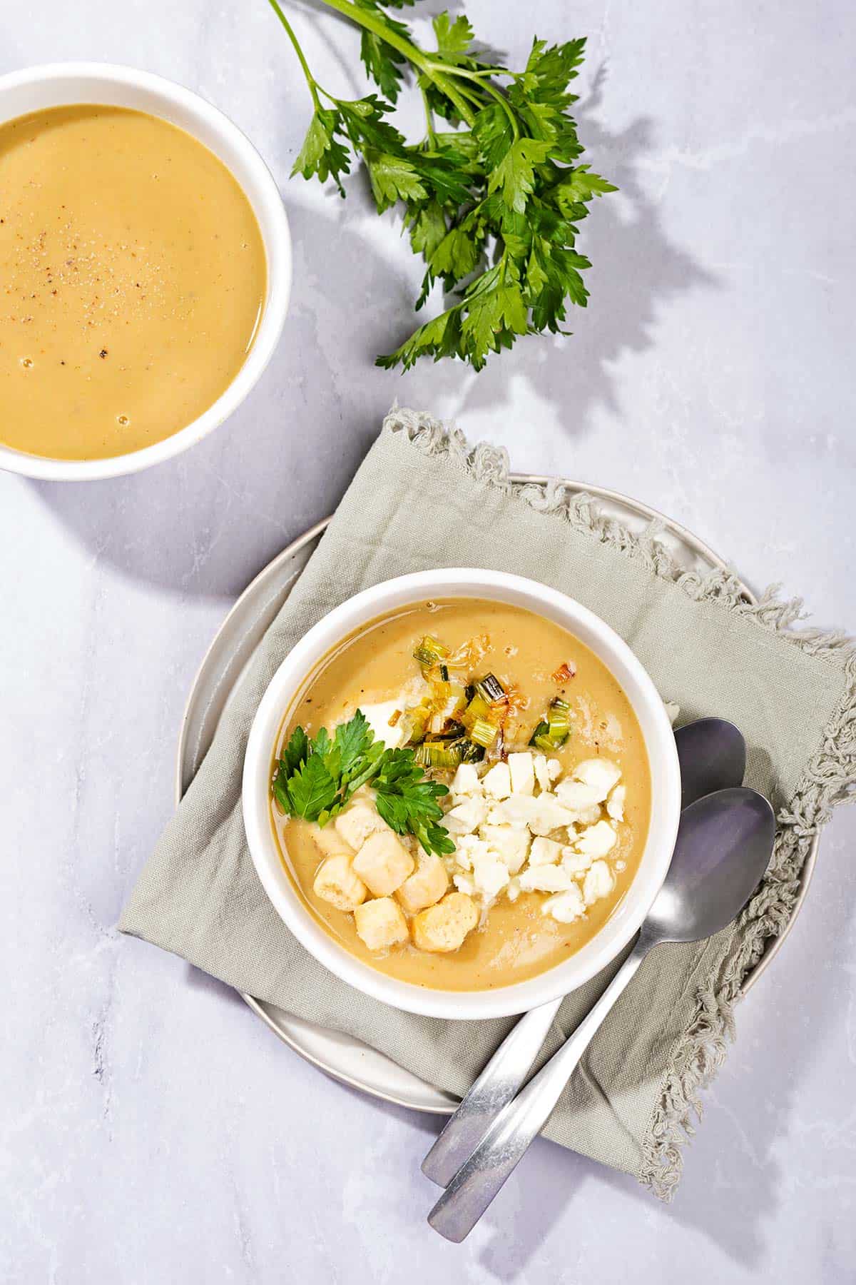 Leek and potato soup topped with croutons, sour cream and parsley leaves served in a bowl, photographed from a bird's eye view. | Hurry The Food Up