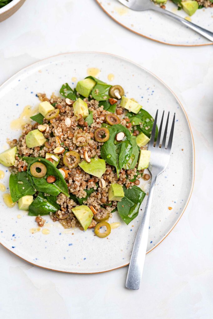 The salad is served on two plates with forks and a small bowl of olive oil and a bowl with spinach that are on the white table | Hurry The Food Up