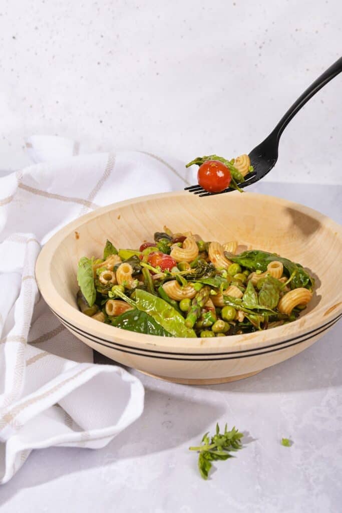 A forkful of pasta salad is lifted from a bowl of pasta salad on a grey surface beside a kitchen towel | Hurry The Food Up