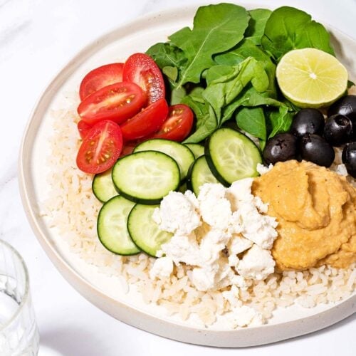 Mediterranean Rice Bowl is served on the plate with a glass of water and tahini sauce in the bowl | Hurry The Food Up