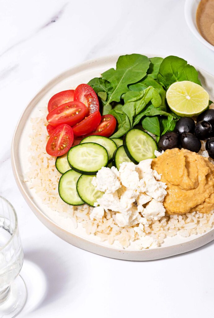 Mediterranean Rice Bowl is served on the plate with a glass of water and tahini sauce in the bowl | Hurry The Food Up