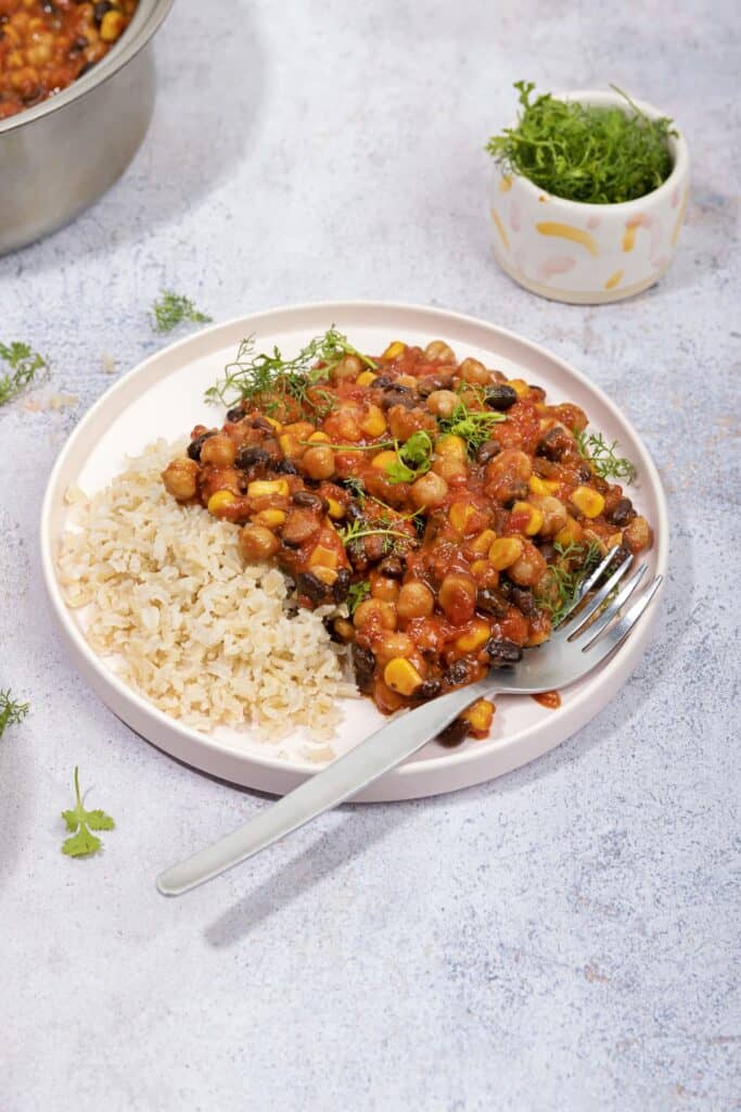 A plate of Mexican bean stew on a grey surface. A pot of cilantro is next to it, to use as garnish. | Hurry The Food Up