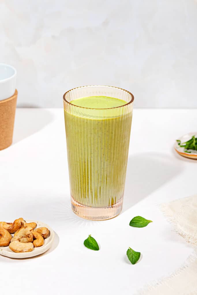 A tall glass of smoothie with torn mint leaves next to it and two small trays, of cashews & mint | Hurry The Food Up