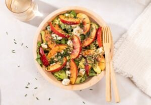 Birdeye view of the nectarine salad that is in the wooden bowl with wooden spoon and fork in it. There are a glass of water and white cloth | Hurry The Food Up