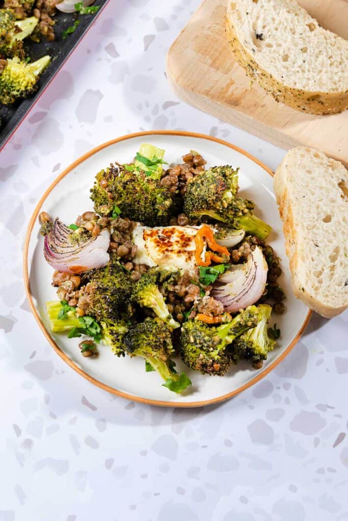 The Oven Roasted Broccoli Halloumi is served on a white plate next to the baking tray and wooden board with bread slices | Hurry The Food Up