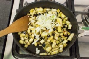 Aubergines and onion in a frying pan with a wooden spatula for stirring them, being fried up for sauce| Hurry The Food Up