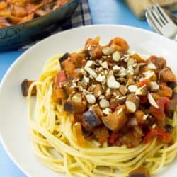 A plate of pasta arrabbiata on a blue surface. A board and a pan full of the sauce are in the corner | Hurry The Food Up