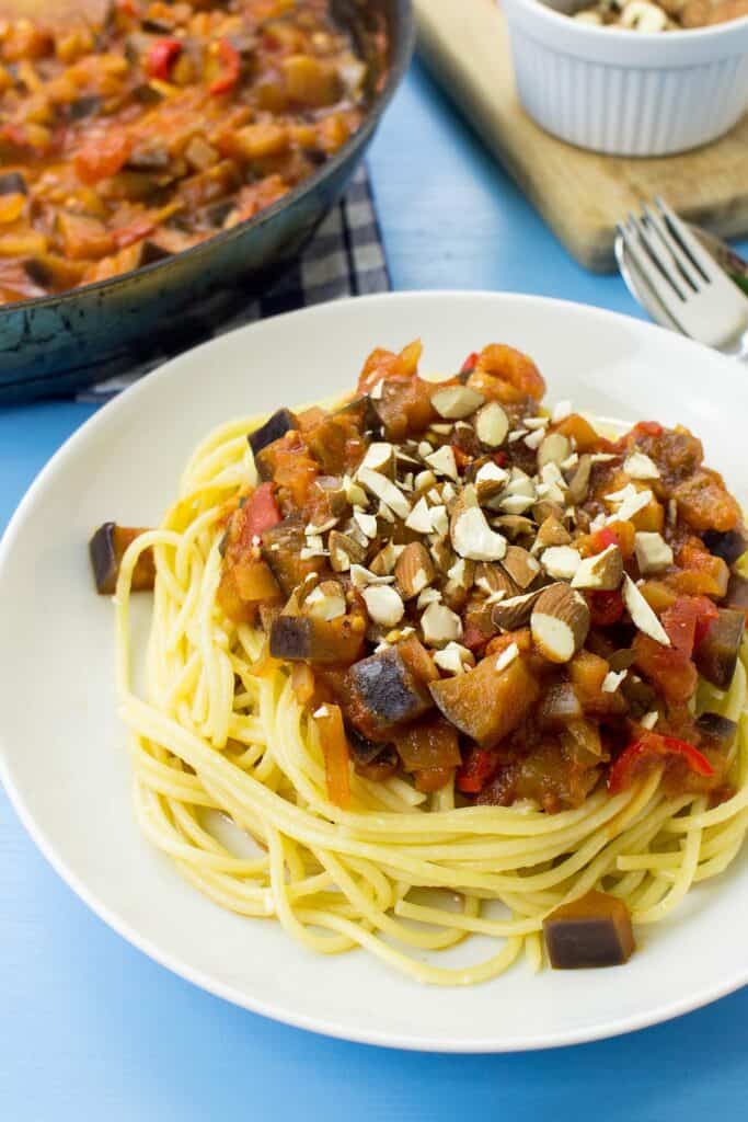 A plate of pasta arrabbiata on a blue surface. A board and a pan full of the sauce are in the corner | Hurry The Food Up