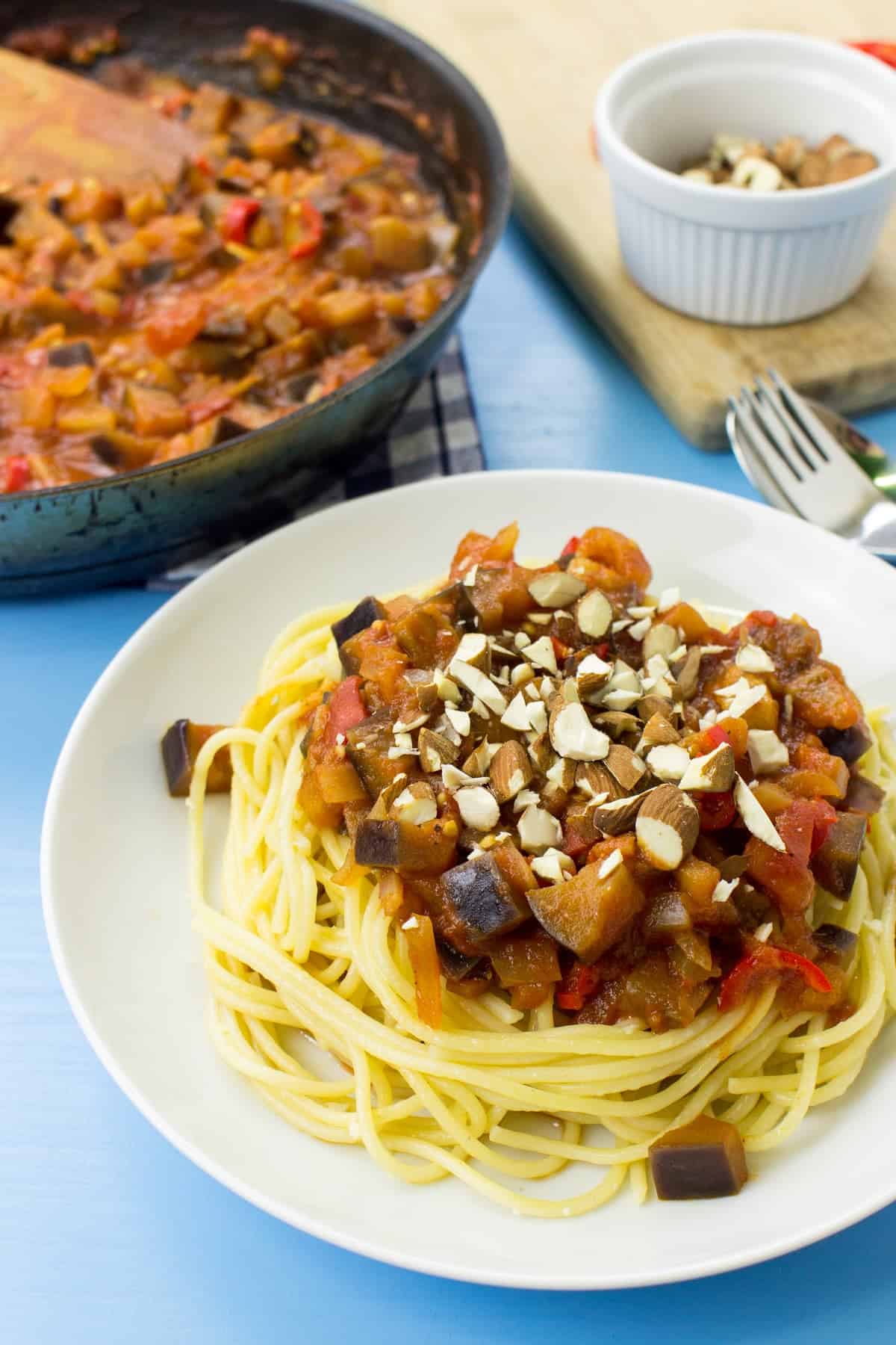 A plate of pasta arrabbiata on a blue surface. A board & a pan full of the sauce are in the corner | Hurry The Food Up