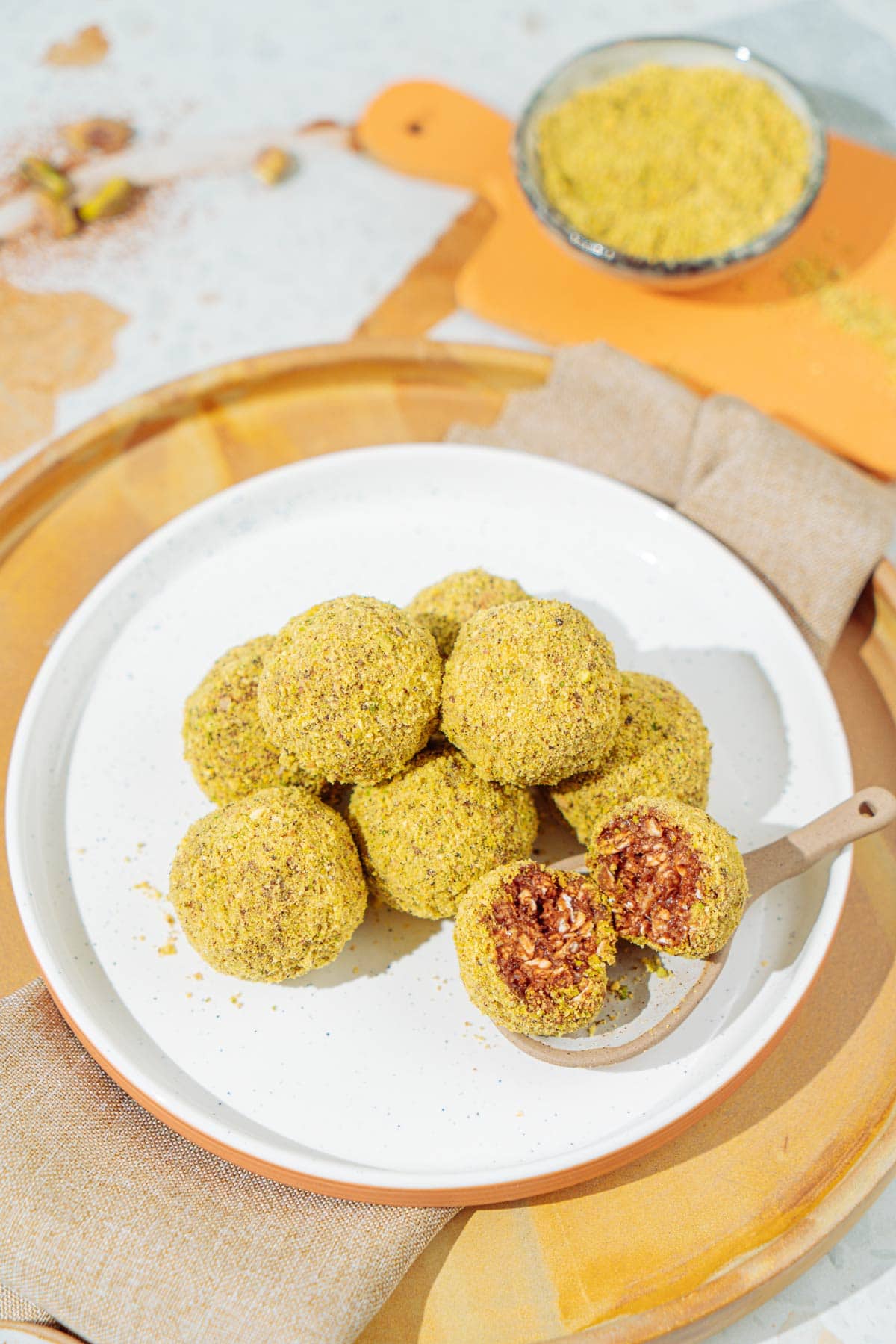 A white plate with peanut butter protein balls that is is on the wooden tray with linen napkin under it. Near it there is a small bowl with ground nuts | Hurry The Food Up