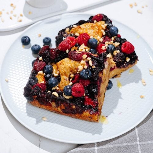 A nice white plate with French toast is on a light surface. Next to it, there are grey napkin, two forks and a white tray with honey and chopped nuts | Hurry The Food Up