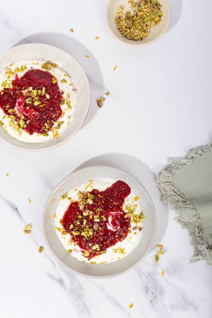 Two bowls of yogurt with compote, sprinkled with pistachios. A small bowl of pistachios in the corner | Hurry The Food Up