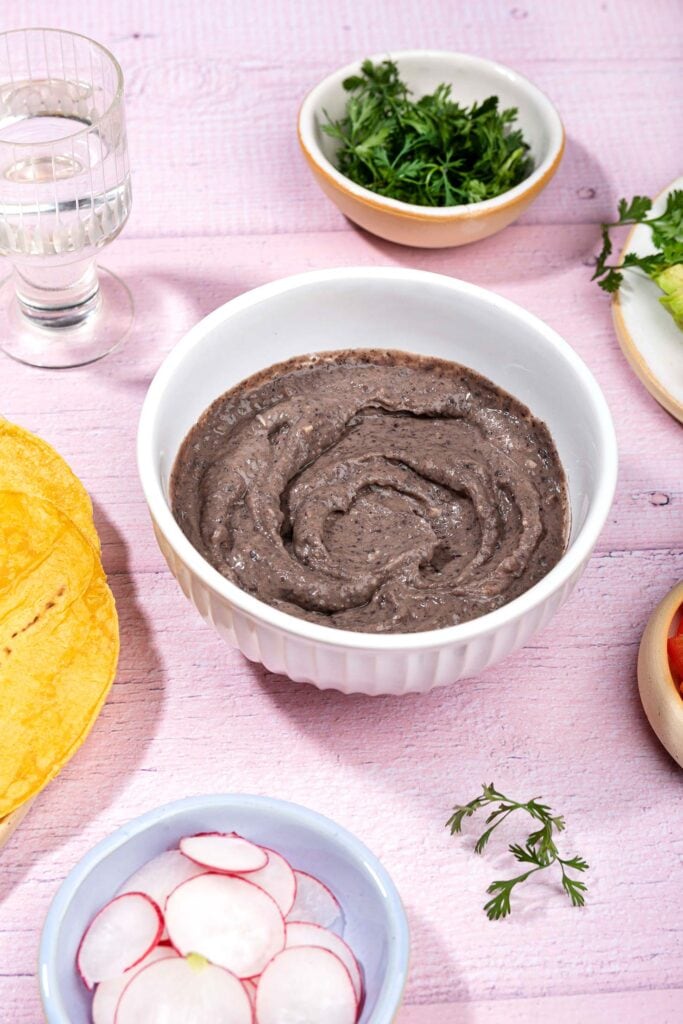 Refried beans are served in the white bowl that is on the table with tortillas, cilantro, sliced radishes etc.| Hurry The Food Up