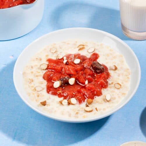 A bowl of rhubarb and bulgur porridge, with plates of sugar, chopped almonds, pot with topping and a glass of milk | Hurry The Food Up