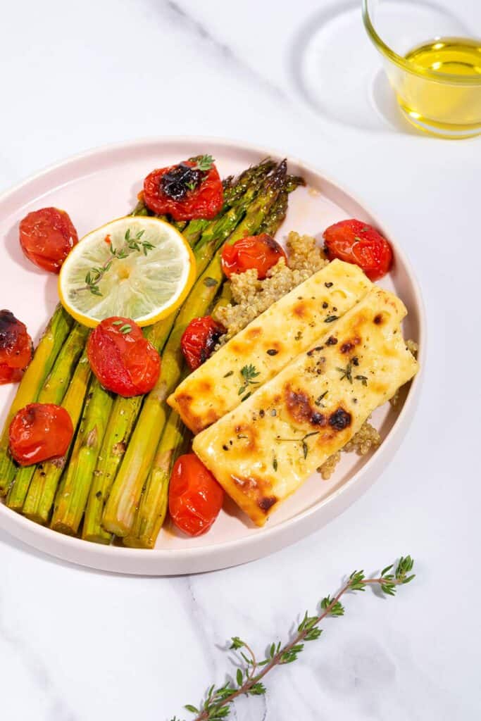 A plate of roast asparagus, halloumi and tomatoes, on a bed of quinoa with a jar of olive oil in shot | Hurry The Food Up