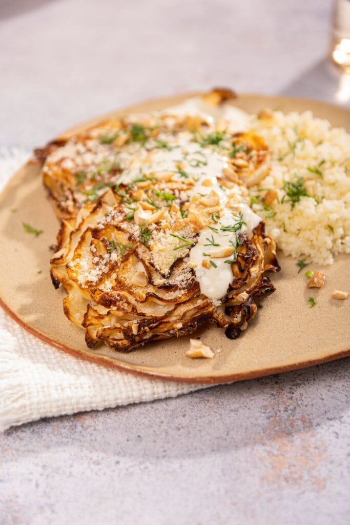 cabbage steaks topped with panko breadcrumbs on a ceramic plate. Sitting on a cream cloth on top of a stone table | Hurry The Food Up