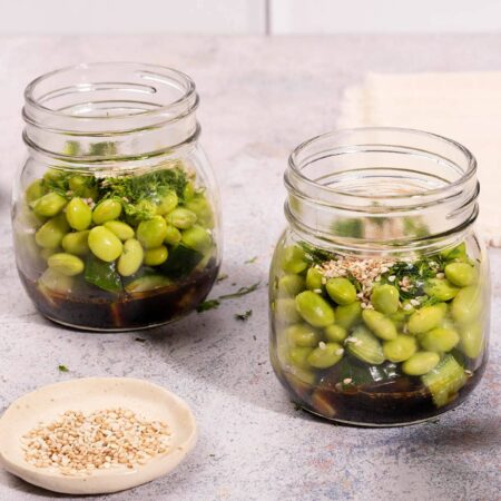 On a stone table sits two mason jars containing cucumber and edamame smashed salad | Hurry The Food Up