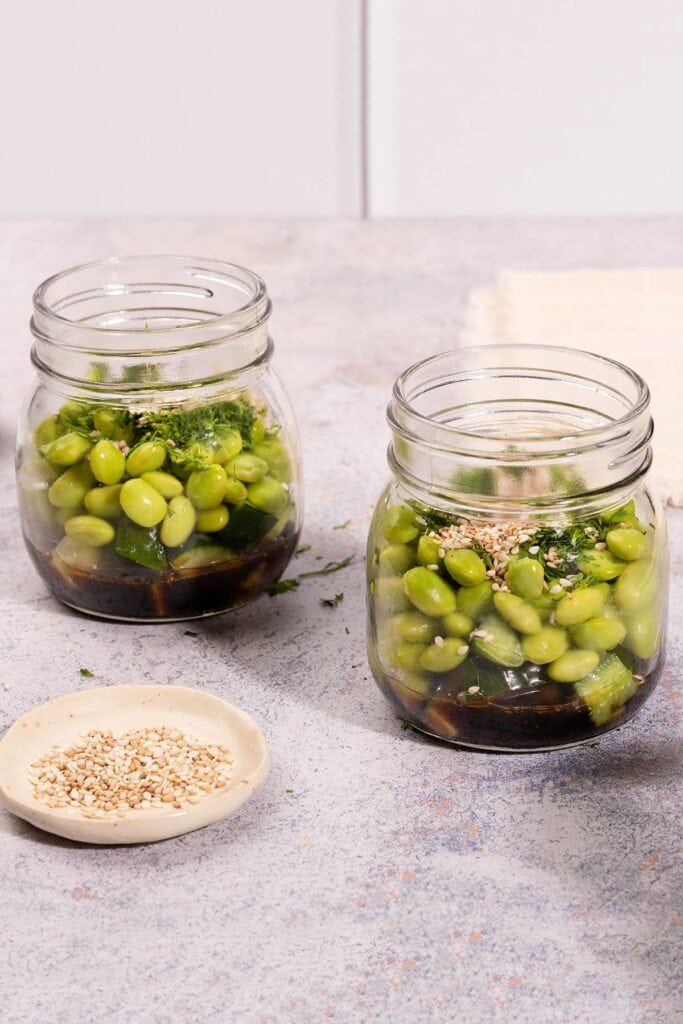 On a stone table sits two mason jars containing cucumber and edamame smashed salad | Hurry The Food Up