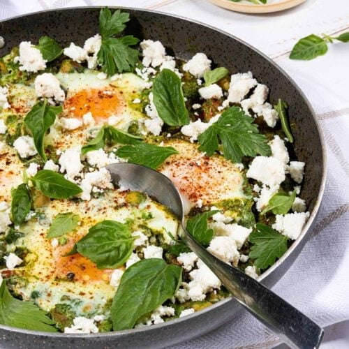 Spinach and Chickpea Bake is ready in the pan with tablespoon that is on the white towel and white table with a small plate of greens | Hurry The Food Up