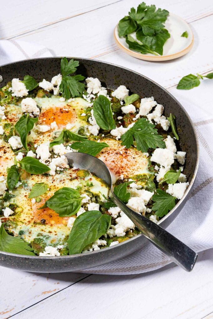 Spinach and Chickpea Bake is ready in the pan with tablespoon that is on the white towel and white table with a small plate of greens | Hurry The Food Up