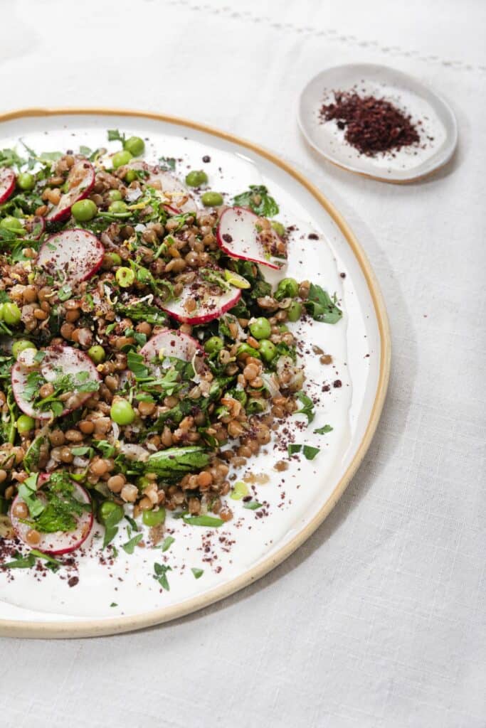 A plate full of salad on a white surface with a small tray of sumac next to it, taken from a side angle | Hurry The Food Up