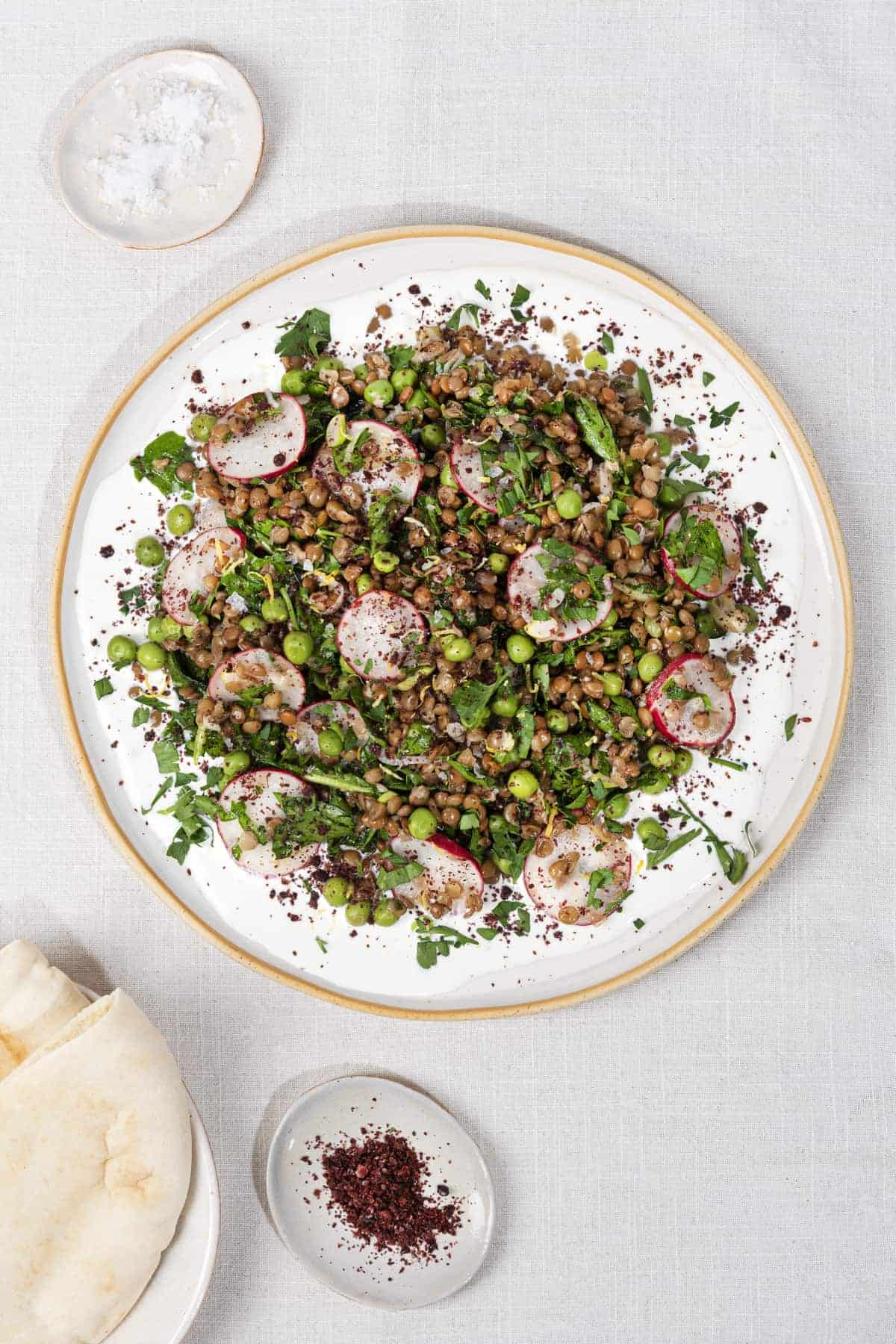 A birds eye view of a plate of salad, with a tray of salt and another of sumac next to it, and flatbreads | Hurry The Food Up