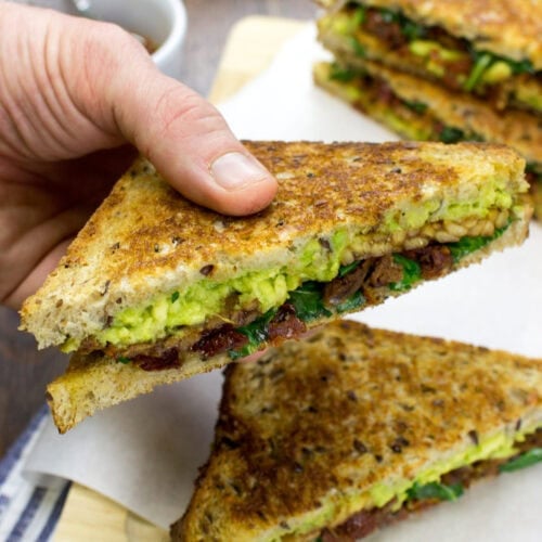 Half of a tempeh sandwich is held up with another below it and two in the distance | Hurry The Food