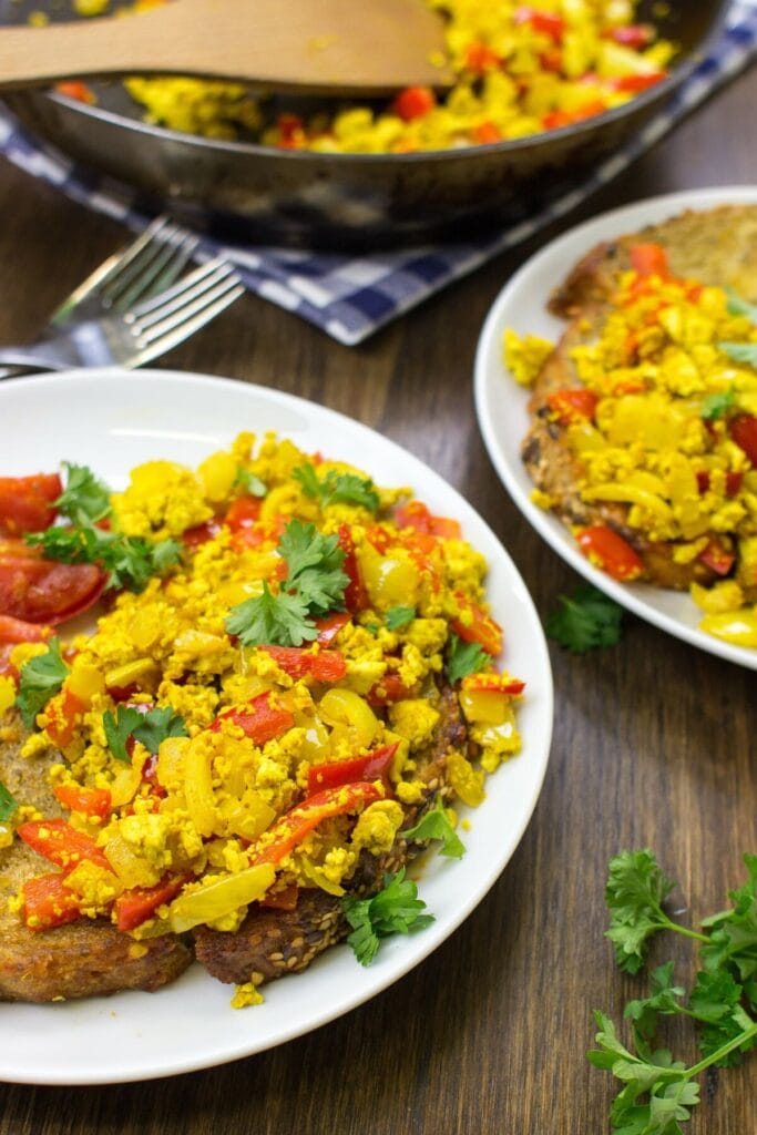 Two plates of scrambled tofu are placed upon a table. A frying pan with tofu scramble is in the distance | Hurry The Food Up