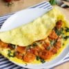 An omelette filled with cheese and tomatoes is served folded on a plate. | Hurry The Food Up