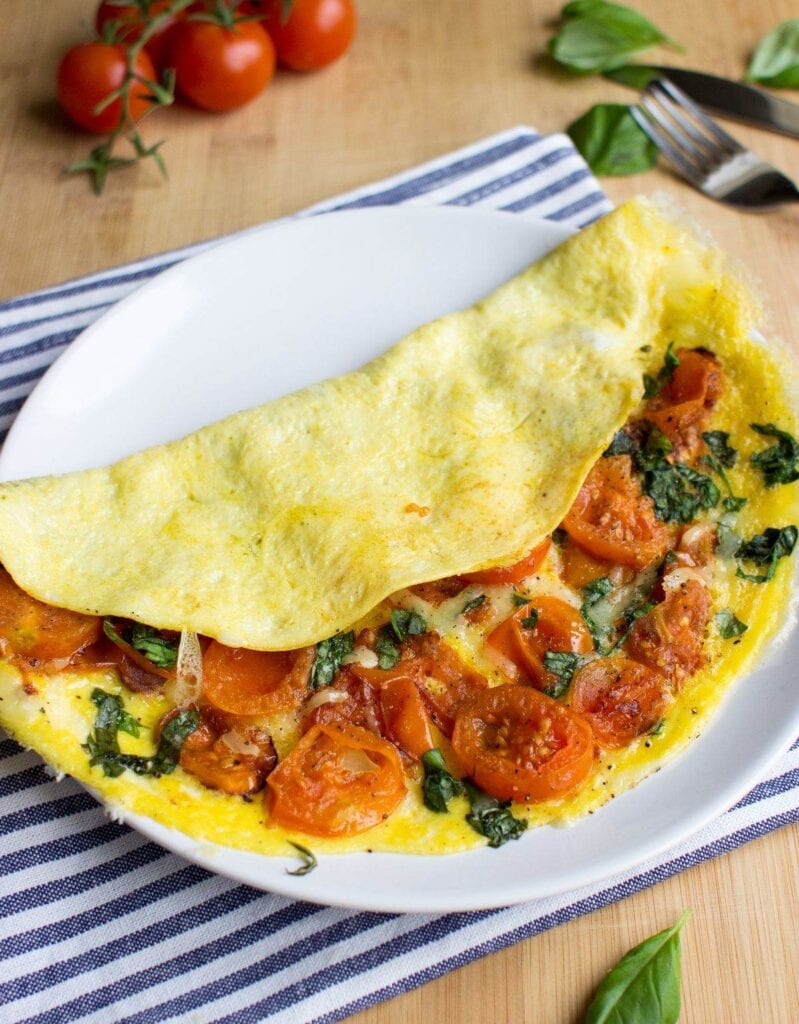 An omelette filled with cheese and tomatoes is served folded on a plate. | Hurry The Food Up