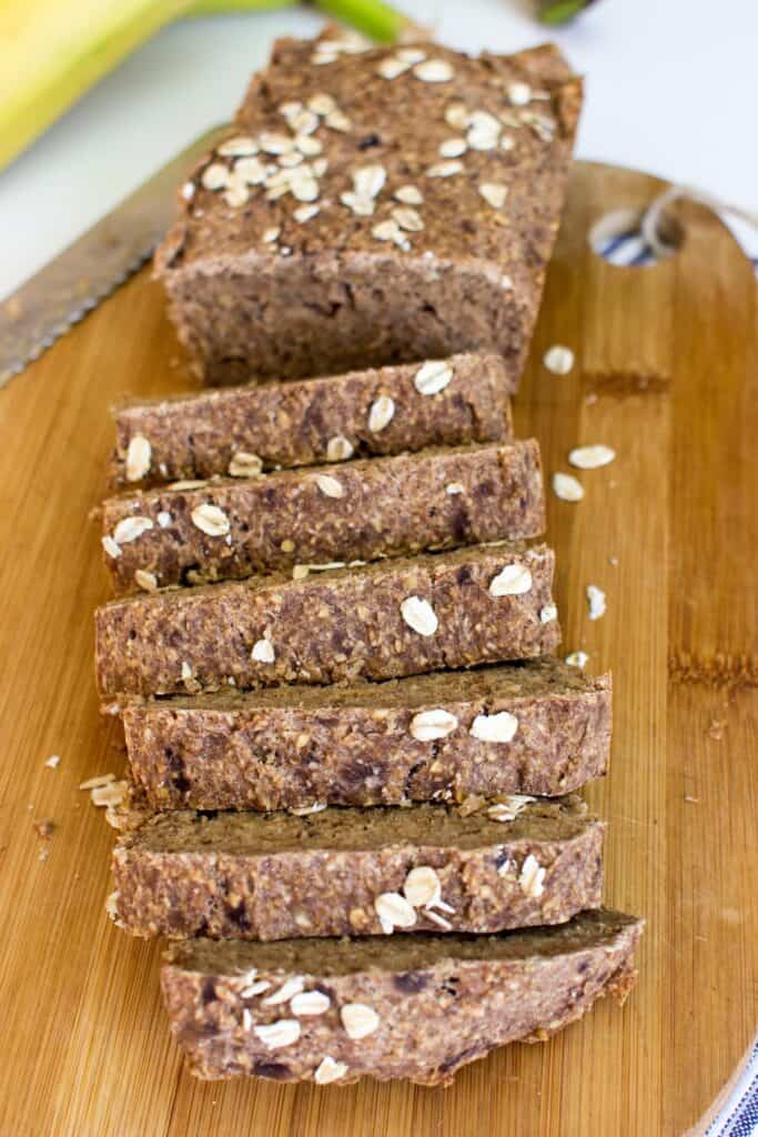 A loaf of banana bread on a wooden chopping board. Half of it has been cut into thick slices | Hurry The Food Up