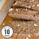 A loaf of banana bread on a wooden chopping board, half cut into generous slices with a time stamp in the bottom left hand corner | Hurry The Food Up