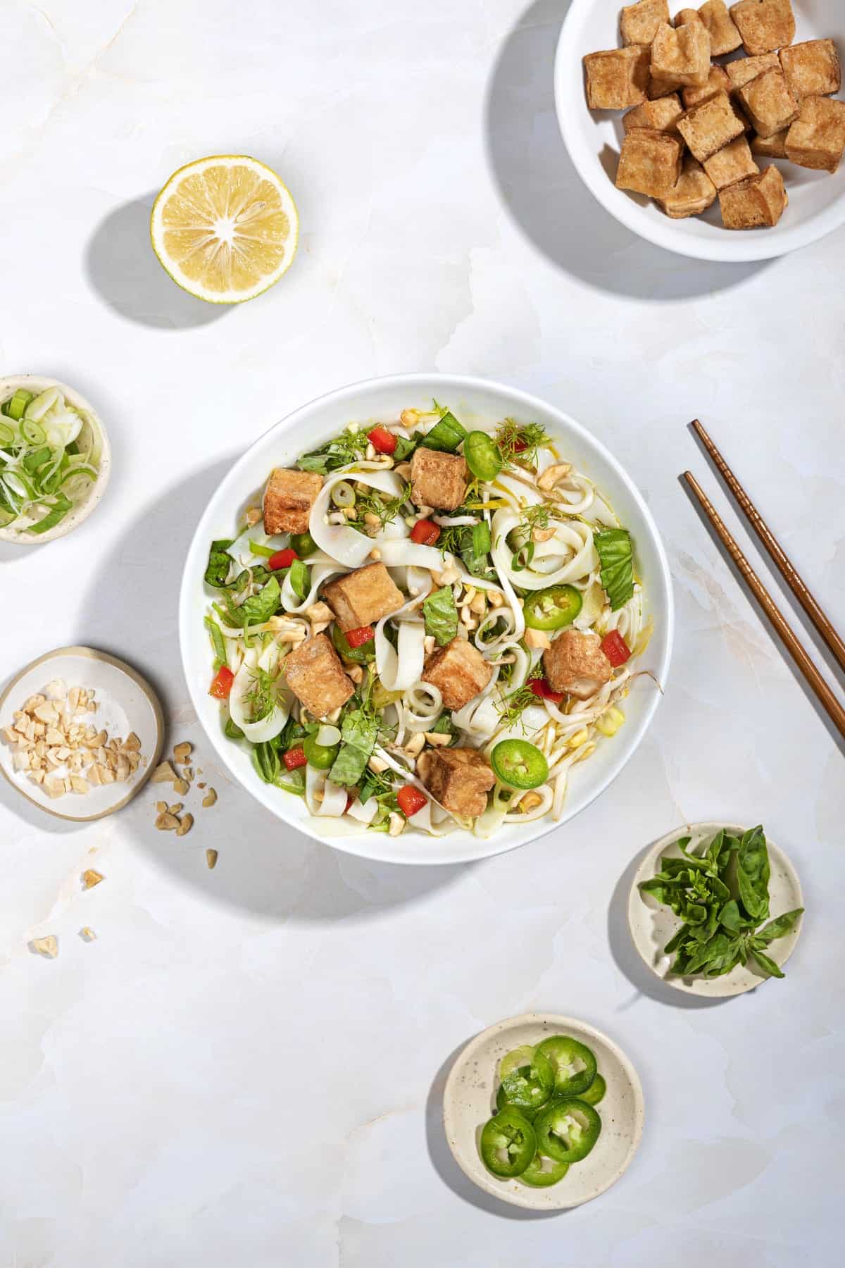 Bird’s eye view of a bowl of pho with smaller plates of toppings and a pair of chopsticks surrounding it | Hurry The Food Up